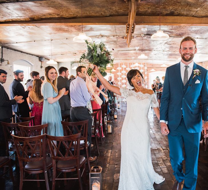 Bride in Lace Watters Dress with Bardot Neckline and Buttons Down Back | Blossom and Bluebird Cathedral Length Veil | Bridal Up Do | Groom in Royal Blue Three-Piece Suit from Moss Bros. with Silver Tie and Pocket Square from T.M.Lewin | Bridal Bouquet of Dusky Pink Roses, White Peonies, Sweetpeas, Coffee-Coloured Phlox and Foliage Tied with Cappuccino Silk Ribbon | Hurricane Lanterns | Wedding Ceremony at The West Mill | Smoke Bombs and Chinese Paper Fans Backdrop with Bride in Bardot Dress | Twig &amp; Vine Photography