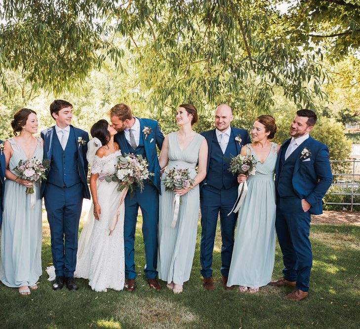 Bride in Lace Watters Dress with Bardot Neckline and Buttons Down Back | Bridal Up Do | Blossom and Bluebird Cathedral Length Veil | Bridesmaids in Sage Green Dresses with Embellished Straps from ASOS | Bridal Bouquet of Dusky Pink Roses, White Peonies, Sweetpeas, Coffee-Coloured Phlox and Foliage Tied with Cappuccino Silk Ribbon | Groom in Royal Blue Three-Piece Suit from Moss Bros. with Silver Tie and Pocket Square from T.M.Lewin | Groomsmen in Royal Blue Moss Bros. Suits with Silver Ties and Pocket Squares from Tie Specialist UK | Dusty Pink and White Buttonholes Wrapped with Cappuccino Silk Ribbon | Smoke Bombs and Chinese Paper Fans Backdrop with Bride in Bardot Dress | Twig &amp; Vine Photography