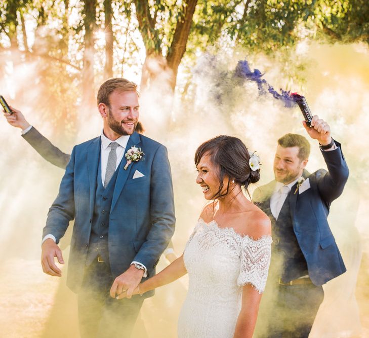 Wedding Party with Colourful Smoke Bombs | Bride in Lace Watters Dress with Bardot Neckline and Buttons Down Back | Bridal Up Do | Groom in Royal Blue Three-Piece Suit from Moss Bros. with Silver Tie and Pocket Square from T.M.Lewin | Bridesmaids in Sage Green Dresses with Embellished Straps from ASOS |  Smoke Bombs and Chinese Paper Fans Backdrop with Bride in Bardot Dress | Twig &amp; Vine Photography