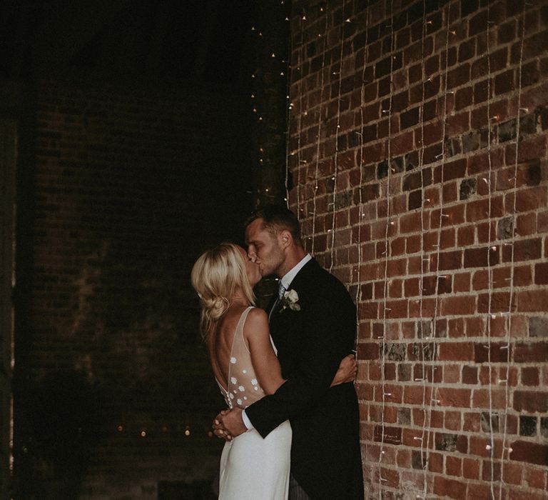 Picture of  Bride in Rime Arodaky Wedding Dress with Lace Inserts and Groom in Morning Suit next to Fairy Lights