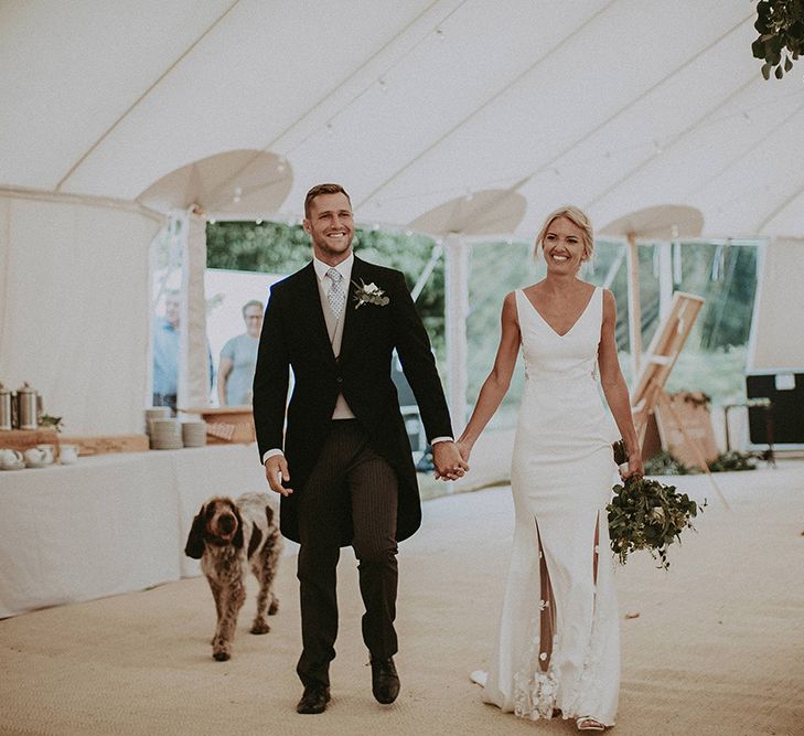 Bride in Rime Arodaky Wedding Dress with Lace Inserts and Groom in Morning Suit Entering The Sperry Tent Reception with Their Dog