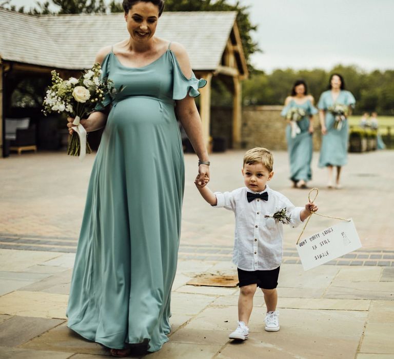 Pregnant bridesmaid with cute pageboy carrying wedding sign