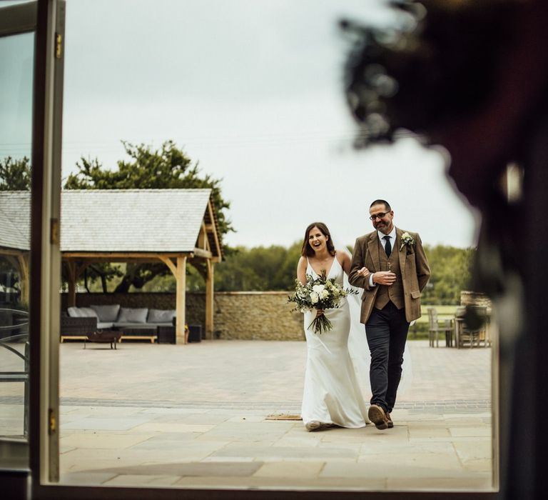 Bride makes entrance at Oxfordshire barn wedding ceremony with father