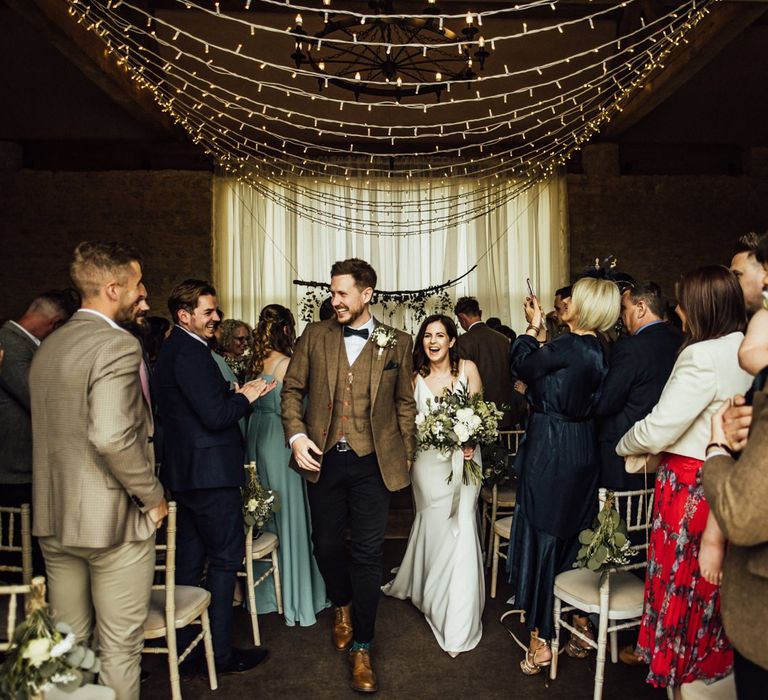 Bride and groom walk back down aisle as husband and wife under fairy light canopy