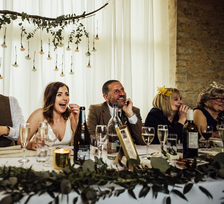 Bride and groom enjoys wedding speeches with flowers hanging behind them