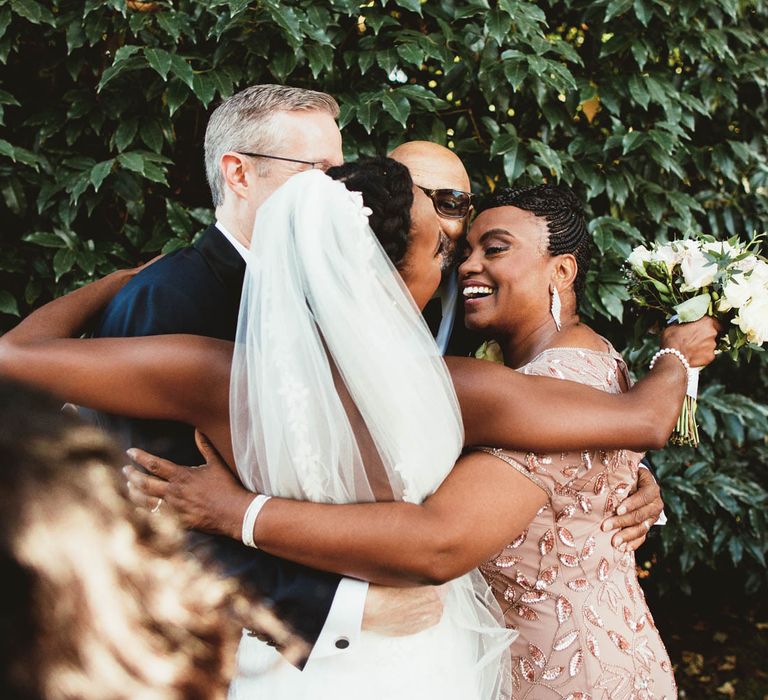 Bride, groom and parents having a group hug after the wedding ceremony