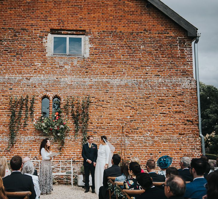 Bride in Halfpenny London Separates of Laura Top with Cowl Back and Long Sleeves, Silk Cami and Laser Cut Palm Skirt | Groom in Navy Tweed Suit by Walker Slater with Yellow Tie and Patterned Pocket Square | Outdoor Wedding Ceremony at Abbey Hall Creative Space | 'Frida Kahlo' Flower Crown, Halfpenny London Bridal Separates and Colourful Bouquets with Peonies for Suffolk Wedding | From The Smiths Photography