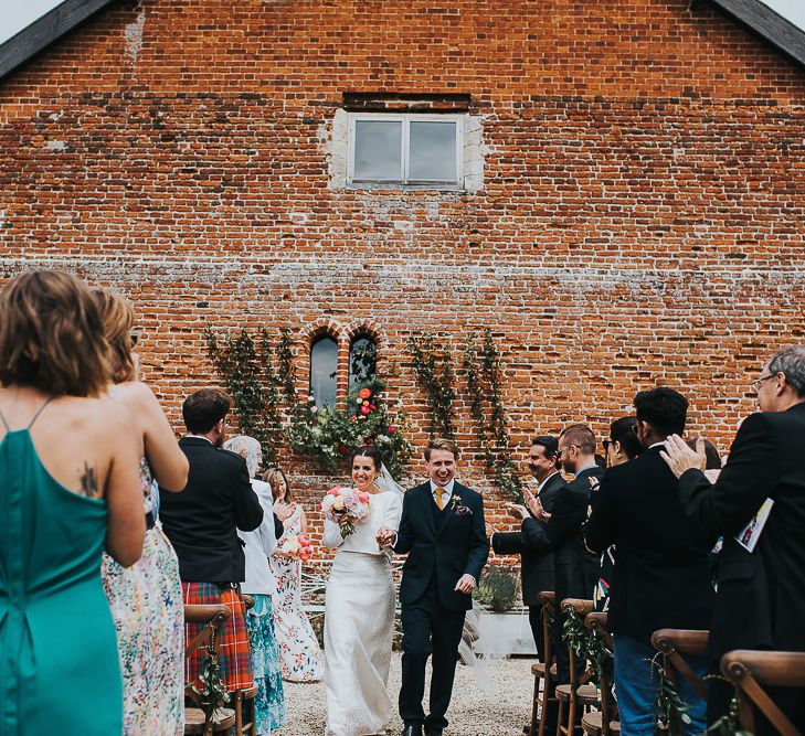 Bride in Halfpenny London Separates of Laura Top with Cowl Back and Long Sleeves, Silk Cami and Laser Cut Palm Skirt | Groom in Navy Tweed Suit by Walker Slater with Yellow Tie and Patterned Pocket Square | Colourful Bridal Bouquet of Pink and White Peonies | Outdoor Wedding Ceremony at Abbey Hall Creative Space | 'Frida Kahlo' Flower Crown, Halfpenny London Bridal Separates and Colourful Bouquets with Peonies for Suffolk Wedding | From The Smiths Photography