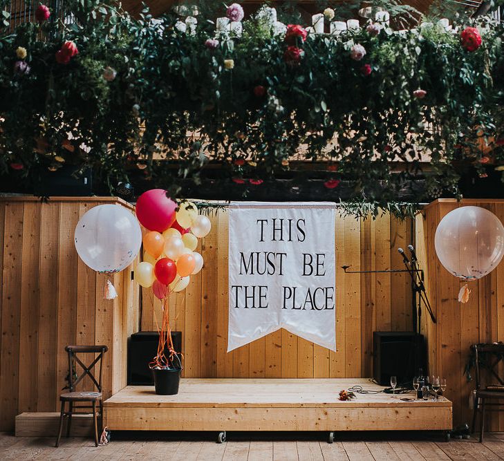 This Must Be The Place Flag | Hanging Floral Installation | Confetti Balloons | Red, Orange and Yellow Balloons | Wedding Reception at Abbey Hall Creative Space | 'Frida Kahlo' Flower Crown, Halfpenny London Bridal Separates and Colourful Bouquets with Peonies for Suffolk Wedding | From The Smiths Photography