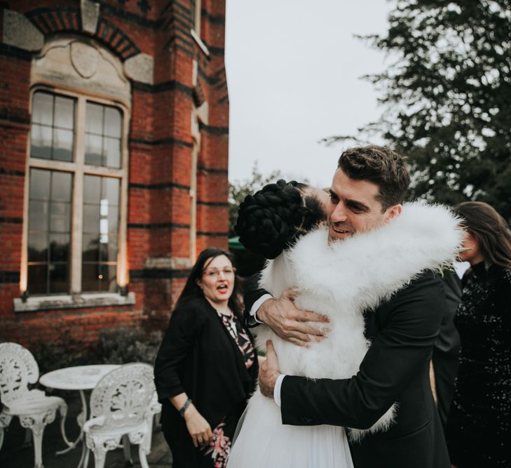 Bride in white faux fur coverup hugging a wedding guest