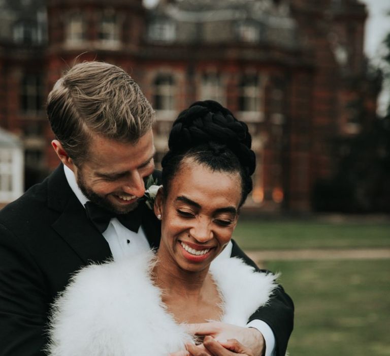 Groom in tuxedo embracing his bride in feather coverup