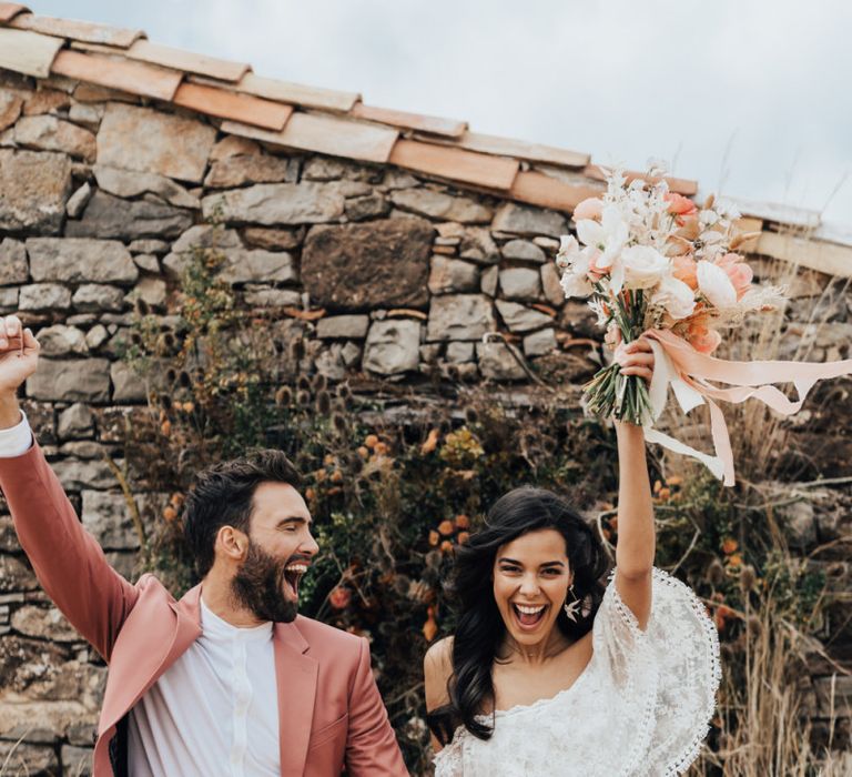 Bride in Grace Loves Lace Wedding Dress and Groom in Dusky Pink Suit Celebrating