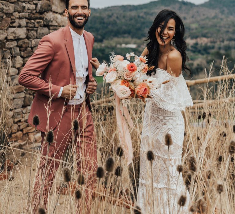 Stylish Bride in Grace Loves Lace Wedding Dress and Groom in Dusky Pink Suit Laughing in the Reeds