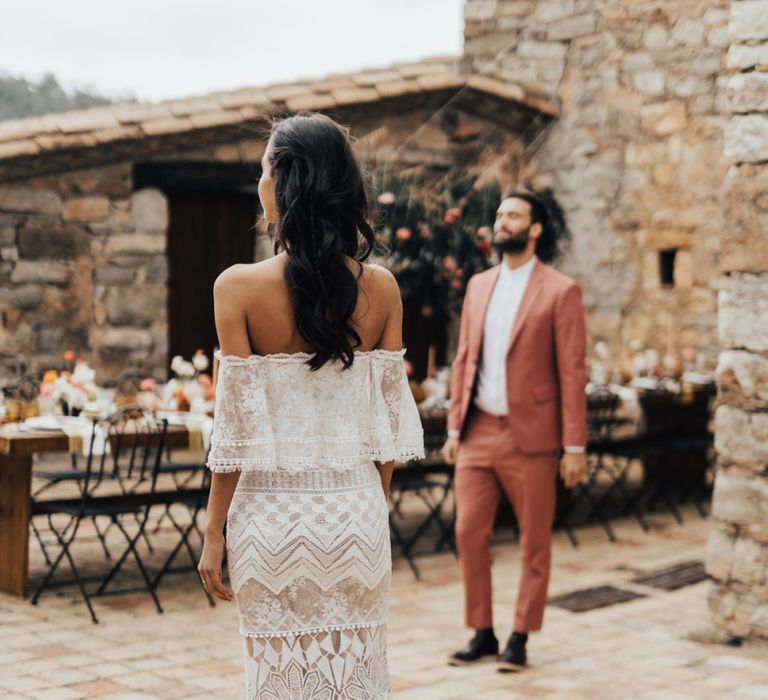 Bride in Bardot Grace Loves Lace Wedding Dress approaching Her Groom for a First Look in a Coral Suit