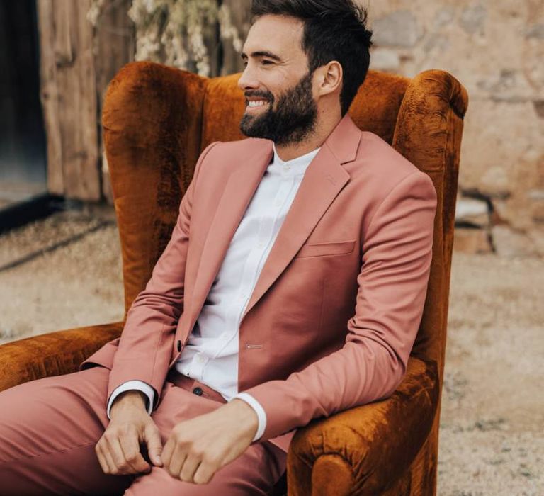 Groom in Coral Suit Sitting on an Armchair