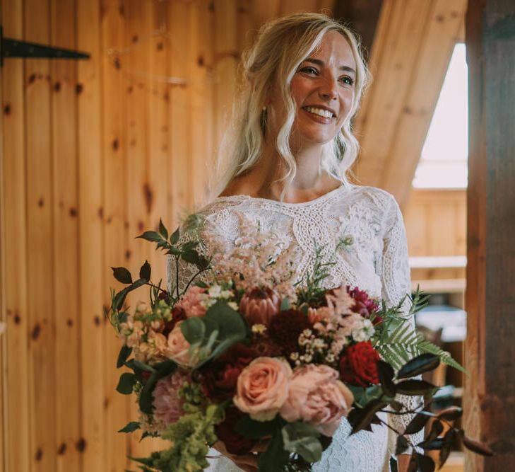 Bride in Grace Loves Lace Inca Gown with Boat Neck, Lace Sleeves and Low Back | Bridal Bouquet of Burgundy and Blush Flowers with Foliage | Mykonos Rewritten Bridesmaid Dresses for an Epic Clifftop Coastal Wedding | Nic Ford Photography