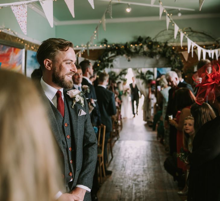 Groom in Three-Piece Grey Herringbone Suit with Burgundy Tie and Buttons | Blush Buttonhole | Foliage Arch | Pastel Bunting | Fairy Lights | Wedding Ceremony at The Druidstone | Mykonos Rewritten Bridesmaid Dresses for an Epic Clifftop Coastal Wedding | Nic Ford Photography