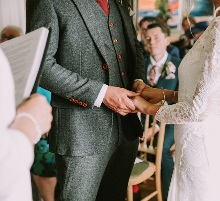 Bride in Grace Loves Lace Inca Gown with Boat Neck, Lace Sleeves and Low Back | Personalised Embroidered Veil by Daisy Sheldon | Groom in Three-Piece Grey Herringbone Suit with Burgundy Tie and Buttons | Wedding Ceremony at The Druidstone | Mykonos Rewritten Bridesmaid Dresses for an Epic Clifftop Coastal Wedding | Nic Ford Photography