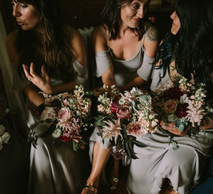 Bridesmaids in Grey Cold Shoulder Dresses by Rewritten | Bouquets of Blush and Pink Flowers with Foliage | Wedding Ceremony at The Druidstone | Mykonos Rewritten Bridesmaid Dresses for an Epic Clifftop Coastal Wedding | Nic Ford Photography