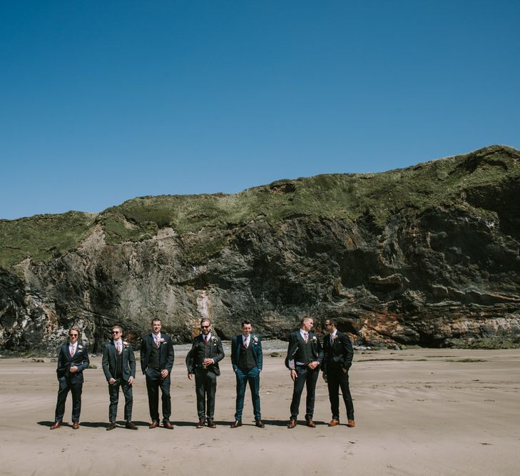 Groom in Three-Piece Grey Herringbone Suit with Burgundy Tie and Buttons | Groomsmen in Mismatched Navy Suits with Blush Pink Ties | Mykonos Rewritten Bridesmaid Dresses for an Epic Clifftop Coastal Wedding | Nic Ford Photography