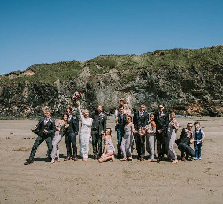 Bride in Grace Loves Lace Inca Gown with Boat Neck, Lace Sleeves and Low Back | Bridesmaids in Grey Cold Shoulder Dresses by Rewritten | Bridal Party Bouquets of Burgundy and Blush Flowers with Foliage | Groom in Three-Piece Grey Herringbone Suit with Burgundy Tie and Buttons | Groomsmen in Mismatched Navy Suits with Blush Pink Ties | Druidston Beach | Mykonos Rewritten Bridesmaid Dresses for an Epic Clifftop Coastal Wedding | Nic Ford Photography