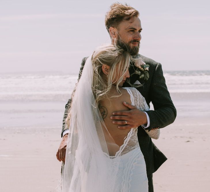 Bride in Grace Loves Lace Inca Gown with Boat Neck, Lace Sleeves and Low Back | Personalised Embroidered Veil by Daisy Sheldon | Aurora Hair Comb by Tilly Thomas Lux | Groom in Three-Piece Grey Herringbone Suit with Burgundy Tie and Buttons | Blush Buttonhole | Druidston Beach | Mykonos Rewritten Bridesmaid Dresses for an Epic Clifftop Coastal Wedding | Nic Ford Photography