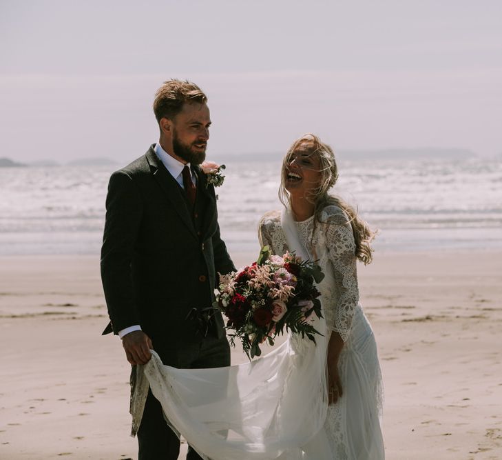 Bride in Grace Loves Lace Inca Gown with Boat Neck, Lace Sleeves and Low Back | Personalised Embroidered Veil by Daisy Sheldon | Groom in Three-Piece Grey Herringbone Suit with Burgundy Tie and Buttons | Blush Buttonhole | Druidston Beach | Mykonos Rewritten Bridesmaid Dresses for an Epic Clifftop Coastal Wedding | Nic Ford Photography