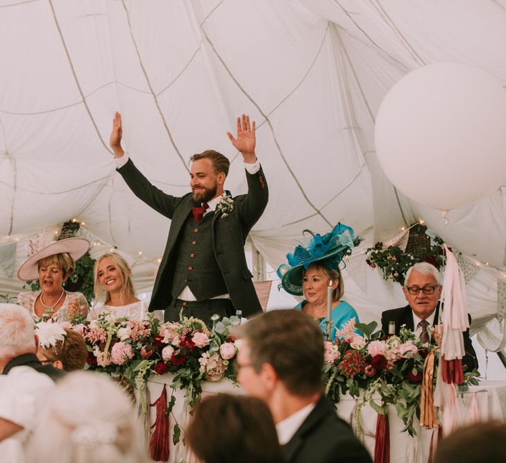 Groom in Three-Piece Grey Herringbone Suit with Burgundy Tie and Buttons | Blush Buttonhole | Marquee with Draped Ceiling at The Druidstone | Top Table Runner of Blush and Burgundy Flowers with Foliage | Pastel Bunting | Fairy Lights | Grey Tapered Candles | Giant White Balloons with Grey, Blush and Burgundy Tassels | Mykonos Rewritten Bridesmaid Dresses for an Epic Clifftop Coastal Wedding | Nic Ford Photography