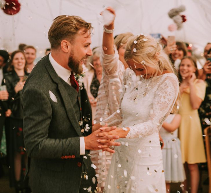 Bride in Grace Loves Lace Inca Gown with Boat Neck, Lace Sleeves and Low Back | Groom in Three-Piece Grey Herringbone Suit with Burgundy Tie and Buttons | Confetti Cannon | First Dance at The Druidstone | Mykonos Rewritten Bridesmaid Dresses for an Epic Clifftop Coastal Wedding | Nic Ford Photography