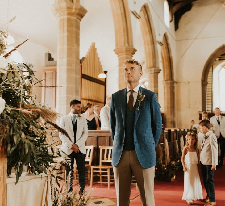 Groom in blue blazer and waistcoat standing at the altar waiting for his bride