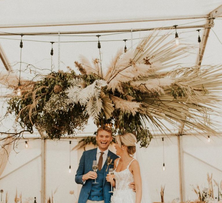 Bride in Galia Lahav wedding dress and groom in blue blazer standing in their boho marquee reception for an August 2020 wedding