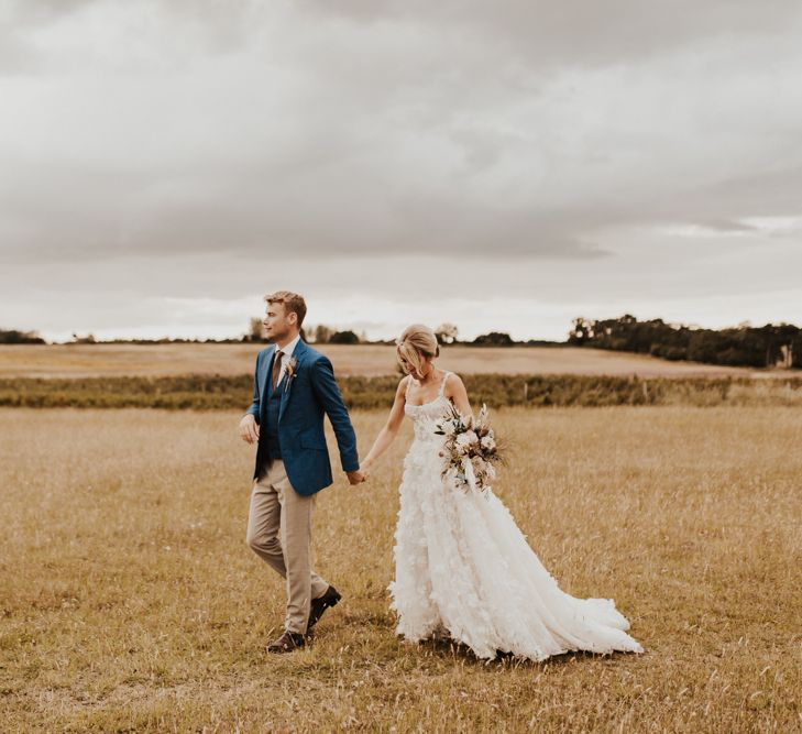 Boho bride and groom walking through the fields at their August 2020 wedding