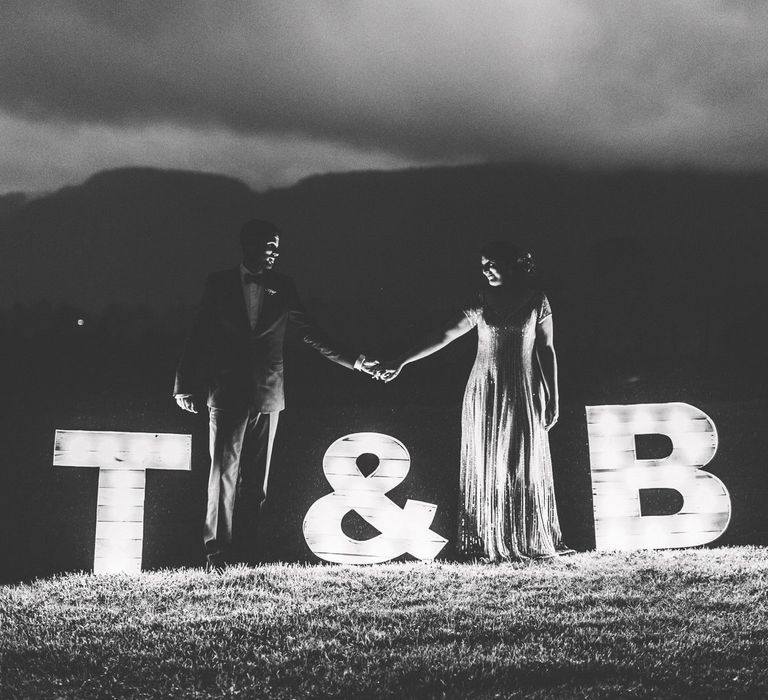 Bride and Groom Standing Next to Giant Initial Lights