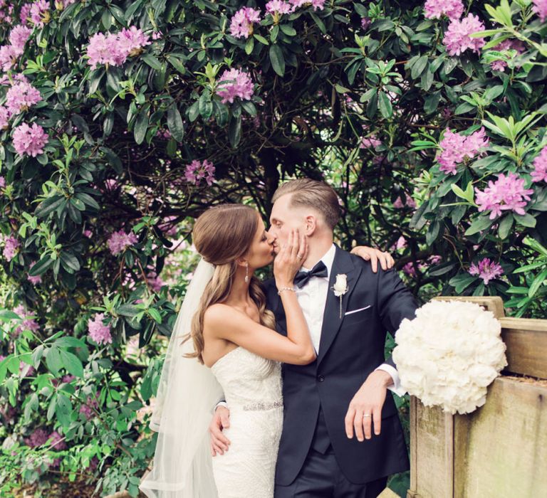 Bride in Beaded Fishtail Wedding Dress Kissing Her Groom in a Black Tie Suit