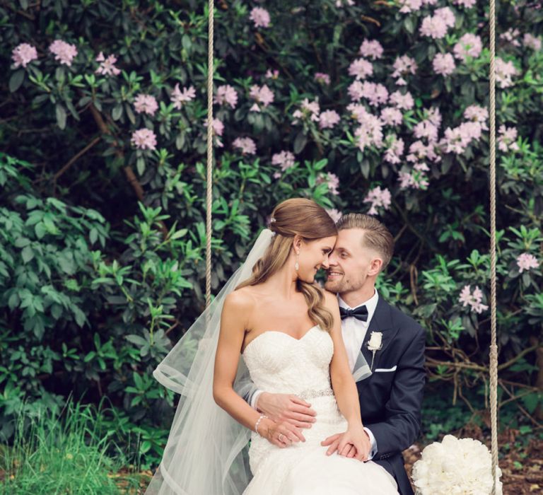 Bride in Beaded Fishtail Wedding Dress and Groom in Gieves &amp; Hawkes Tuxedo Sitting on a Swing