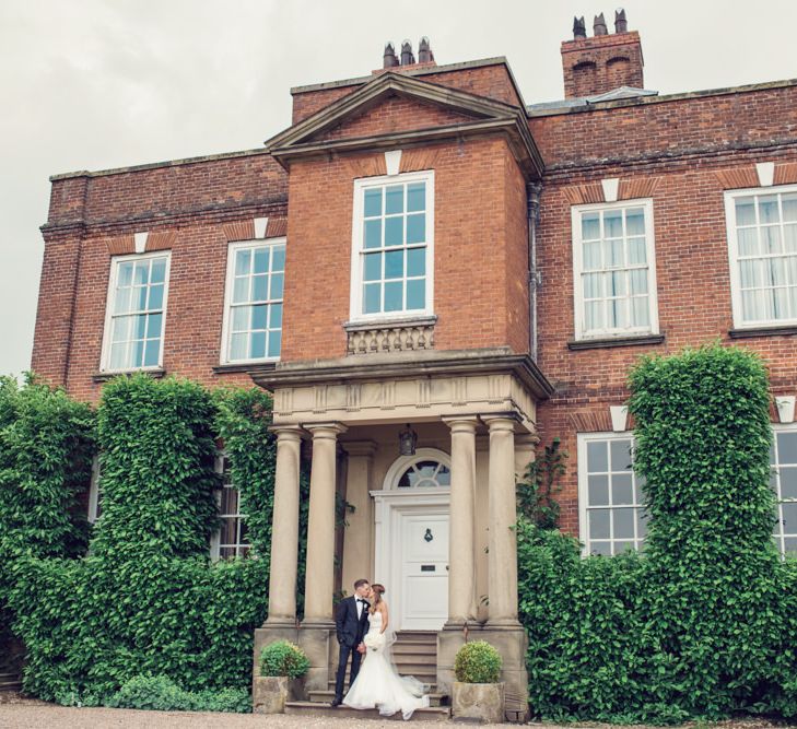 Bride in Beaded Fishtail Wedding Dress and Groom in Gieves &amp; Hawkes Tuxedo Standing at the Entrance to Iscoyd Park Wedding Venue