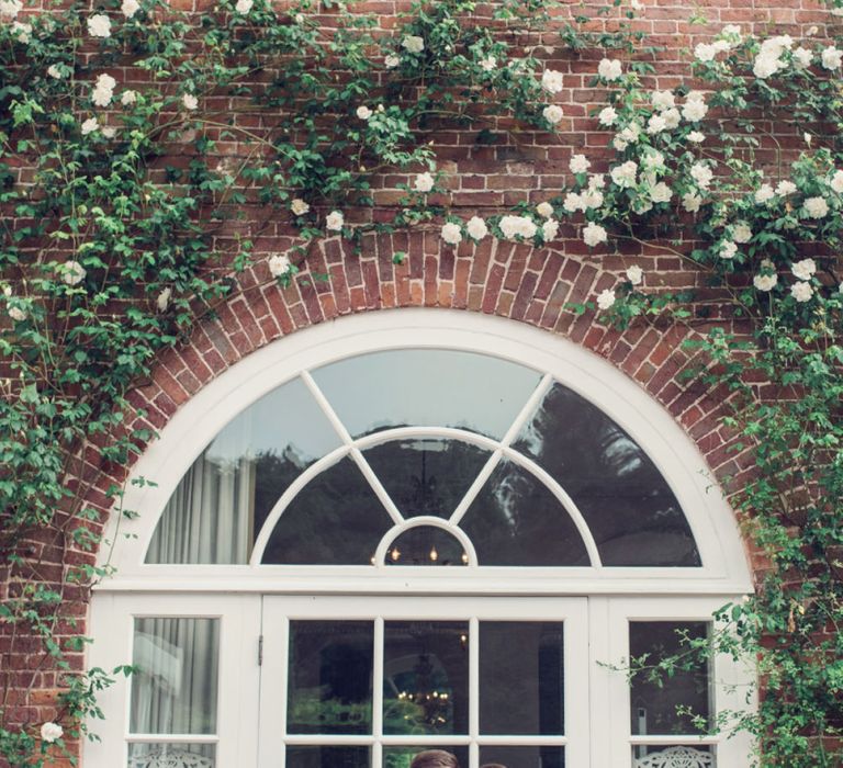 Bride in Beaded Fishtail Wedding Dress and Groom in Gieves &amp; Hawkes Tuxedo Standing in Front of Glass Doors