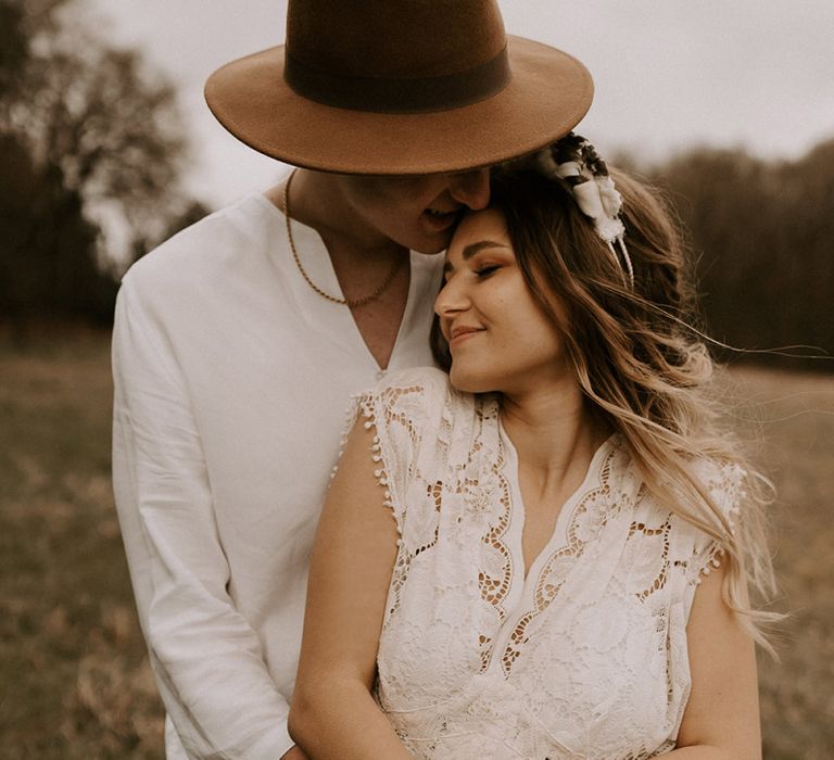 Groom in Fedora Hat Kissing His Boho Bride in a Lace Wedding Dress