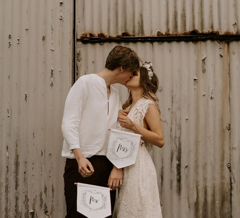 Boho Bride in Lace Wedding Dress and Groom in Casual Trousers and Shirt Holding Up Mr &amp; Mrs Banners