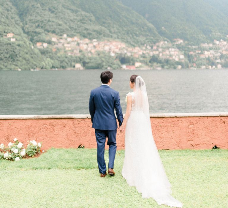 Bride in Fitted Anna Kara Wedding Dress and Groom in Navy Suit Looking Out Over Lake Como