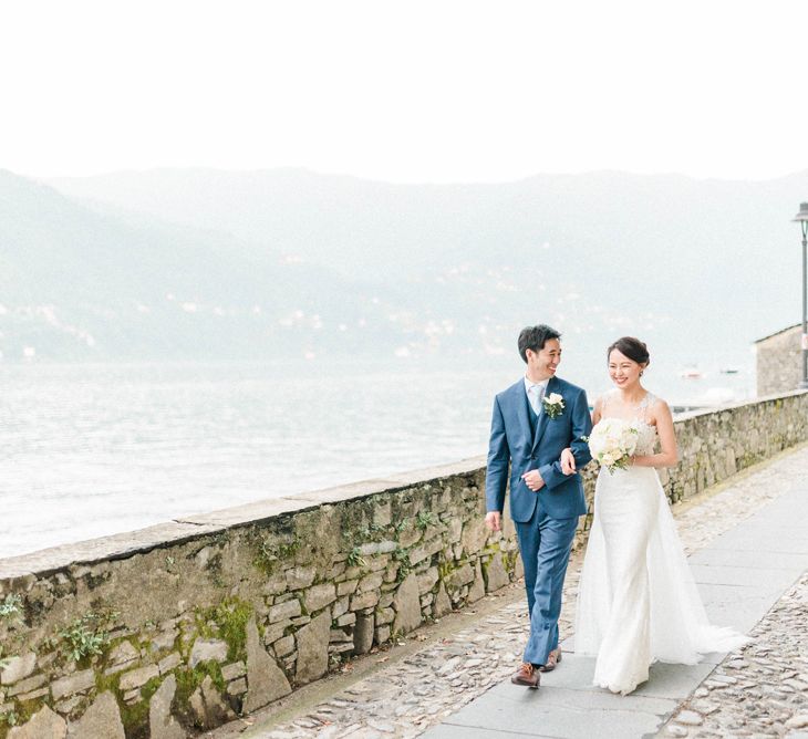 Bride in Anna Kara Wedding Dress and Groom in Three-piece Navy Wedding Suit Walking Next to Lake Como