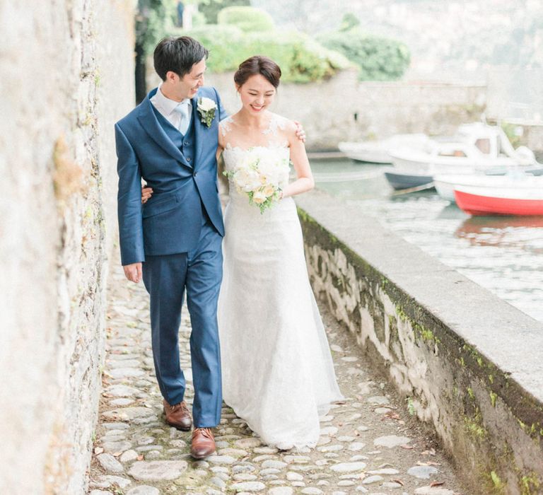 Bride in Anna Kara Wedding Dress and Groom in Three-piece Navy Wedding Suit Arm in Arm