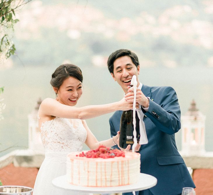 Bride in Anna Kara Wedding Dress and Groom in Three-piece Navy Wedding Suit Popping Champagne and Cutting Their Wedding Cake