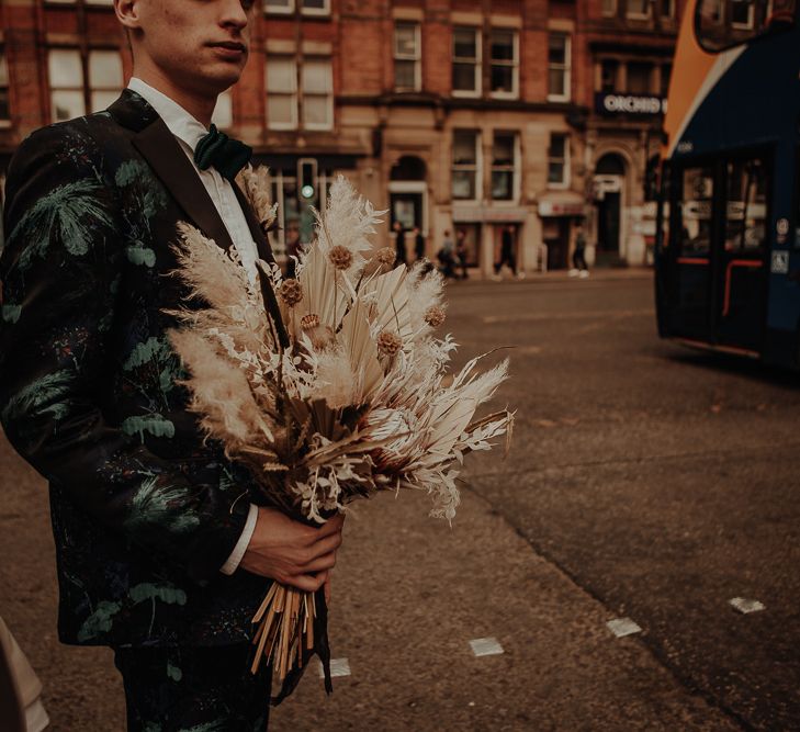 Groom in patterned suit holding a dried flower wedding bouquet