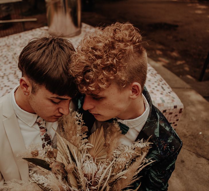 Grooms embracing holding a dried flower bouquet