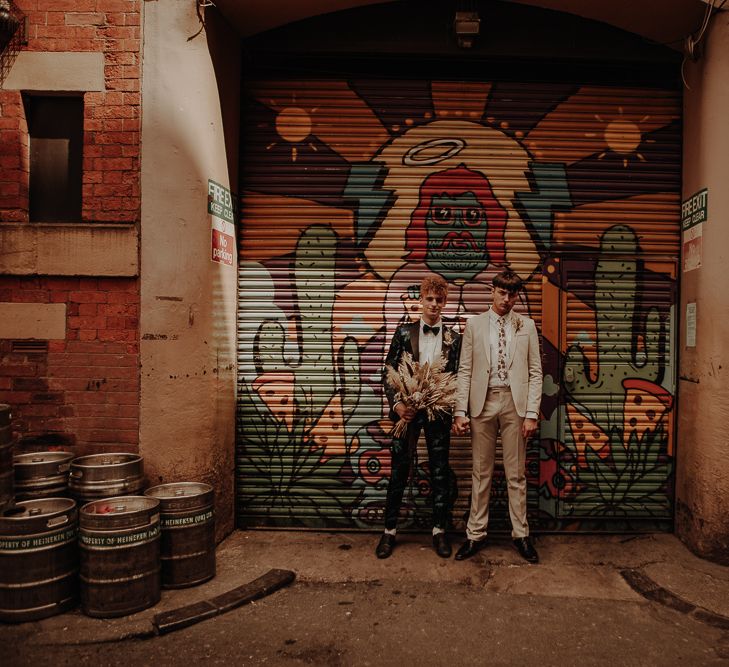 Two grooms standing in front of a shutter covered in graphic art