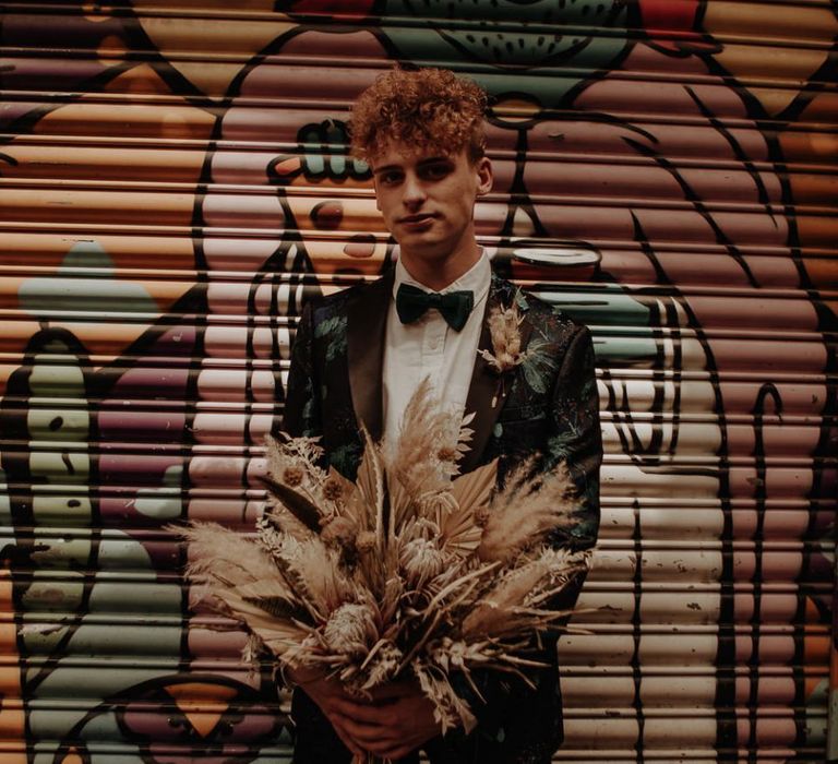 Stylish groom in patterned suit holding a dried flower wedding bouquet