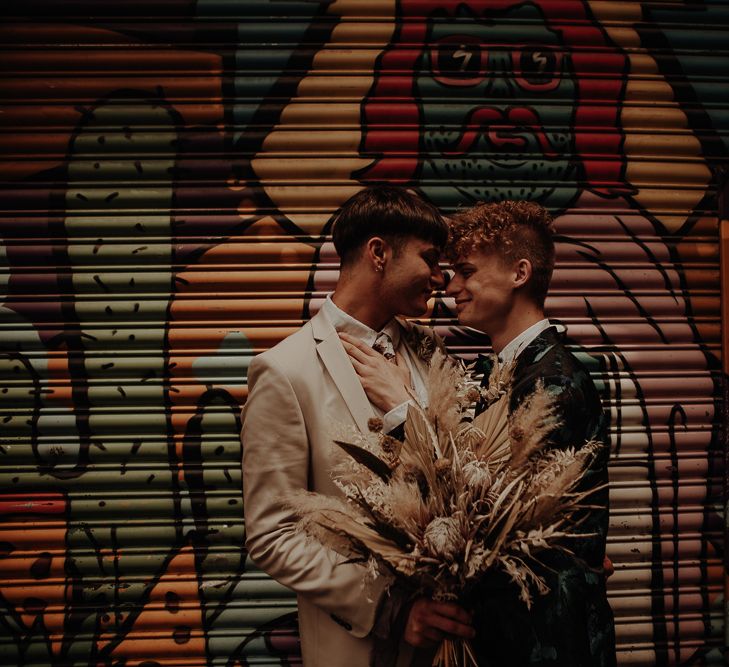 Two grooms standing in front of a shutter decorated in graffiti art