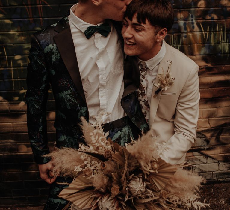 Groom in coloured suit kissing his husband on the head