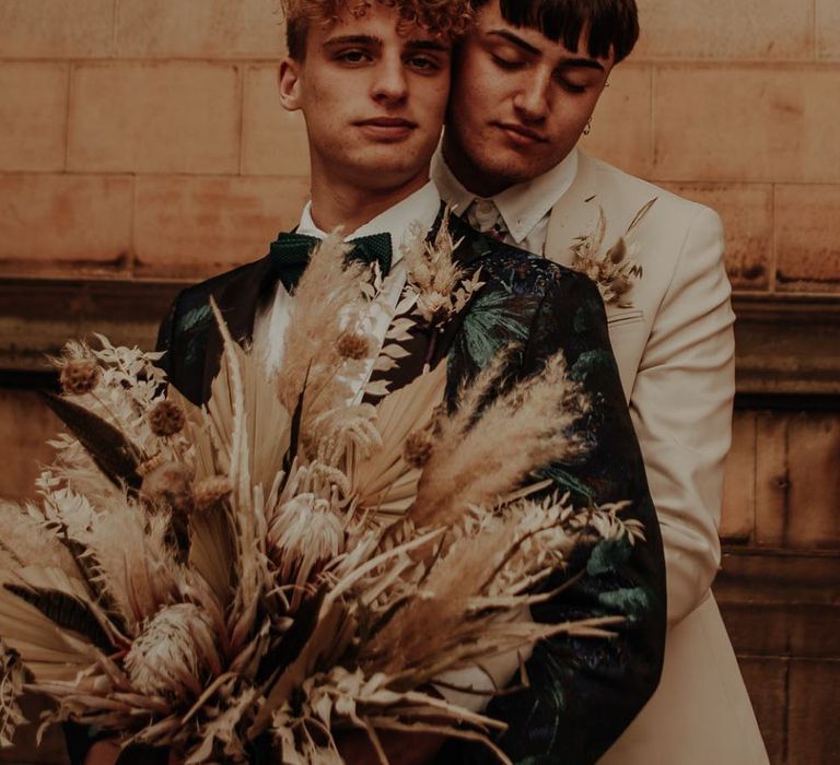 Groom in beige suit embracing his husband in a coloured suit